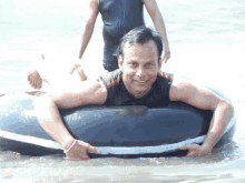 a man in a black tank top is laying on a black inner tube in the water