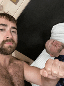 a man with a beard is laying on a bed next to another man without a shirt