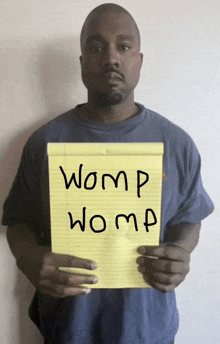 a man in a blue shirt is holding a yellow notepad with the words womp womp written on it