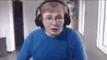 a man wearing headphones and a blue sweater is sitting in front of a window .