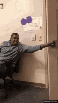 a man is sitting in a chair with his arm outstretched and a purple heart on the wall behind him .