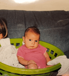 a baby in a pink shirt is in a green laundry basket