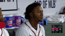 a baseball player sits in the dugout with his eyes closed in front of a bucket of double bubble gum