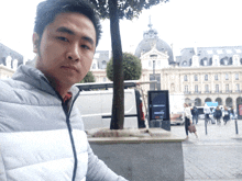 a man in a grey jacket stands in front of a building with a sign that says ' renault ' on it