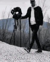a man is walking down a hill with a camera in his hand and says `` no worry i wait '' .