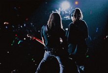 two men playing guitars on a stage with a crowd in the background