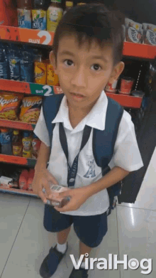 a young boy in a school uniform is standing in front of a shelf that says buy 2 for 2