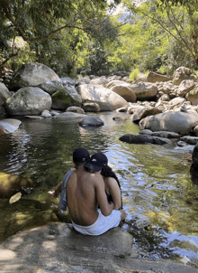 a man and a woman sit on a rock in the water