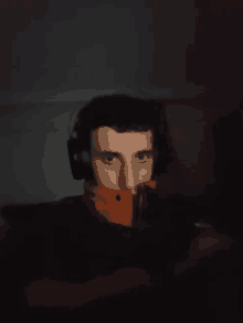 a man wearing headphones and an orange jacket is looking at the camera in the dark .