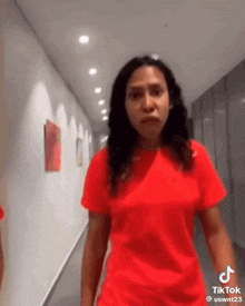 a woman wearing a red shirt is standing in a hallway .