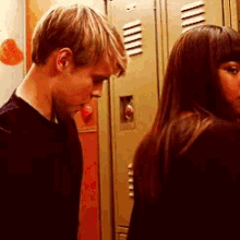 a man and a woman are standing next to each other in front of lockers in a locker room .