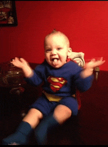 a baby dressed in a superman costume is sitting on a table