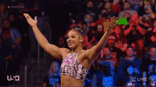 a female wrestler stands in front of a crowd with her arms in the air and a usa logo in the corner