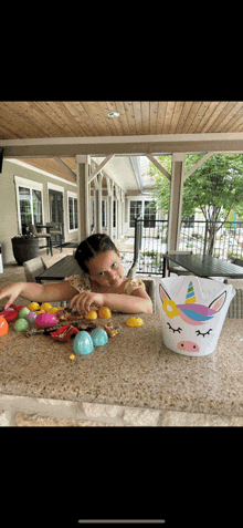 a little girl is sitting at a table with a unicorn bucket