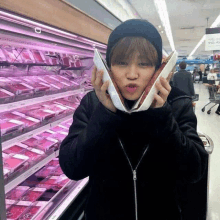 a woman in a black jacket holds a piece of meat in front of a display of meat