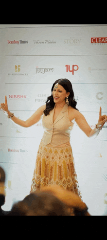 a woman stands in front of a wall of logos including bombay times