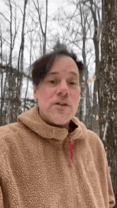 a man wearing a brown jacket is standing in the woods .