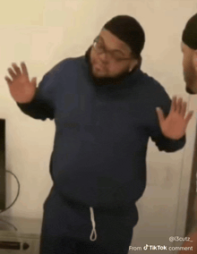 a man in a blue hoodie is standing in front of a wall with his hands outstretched