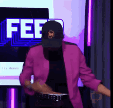 a man wearing a pink jacket and a black hat is dancing in front of a screen that says fee