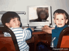 two young boys sit at a desk in front of a computer screen which says " do not disturb " on it