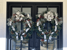 two christmas wreaths are hanging on a glass door