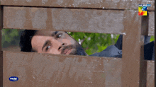 a man is looking through a hole in a wooden fence with hum hd written on the bottom