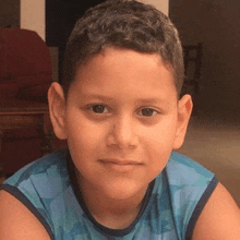 a young boy wearing a blue tank top is looking at the camera and smiling .