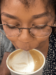 a girl wearing glasses is drinking a cup of coffee