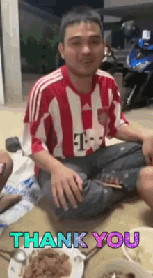 a man in a red and white striped shirt is sitting on the floor next to a plate of food .