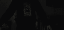 a person is standing in the dark wearing a black sweatshirt with a skull on it .