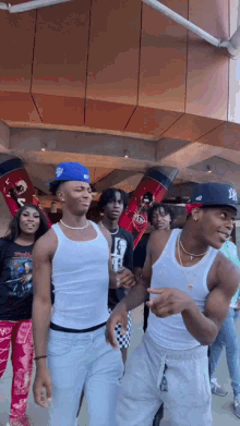 a group of young men are standing in front of a building . one of the men is wearing a la hat .