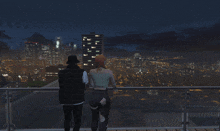 a man and a woman are standing on a balcony looking at a city at night