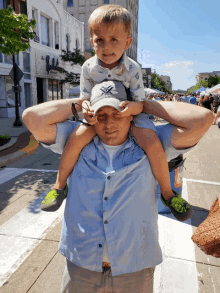 a man is carrying a little boy on his shoulders and the boy is wearing a hat that says vortex on it