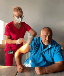 a man in a blue shirt is getting an injection from a woman wearing a mask