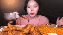 a woman in a pink shirt is eating fried chicken