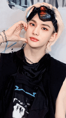 a young man wearing goggles and a necklace is making a heart with his hand