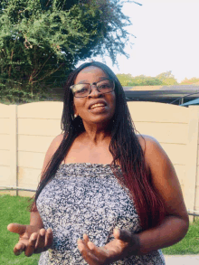 a woman with braided hair and glasses stands in front of a fence