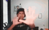 a man is making a heart shape with his hands while wearing a black shirt .