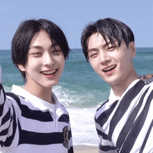 two young men are standing next to each other on the beach and smiling