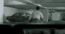 a man in a white shirt is running in a parking garage with cars