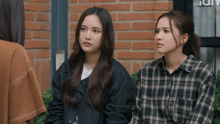 two women sitting next to each other in front of a brick building that says ' city ' on it