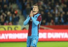 a soccer player wearing a blue and purple jersey with the number 11 on it prays on the field .