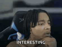 a man with dreadlocks is sitting in a chair and the word interesting is on the screen
