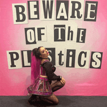 a woman kneeling in front of a pink wall that says beware of the plastics