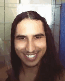 a man with long hair is smiling and looking at the camera in a bathroom .