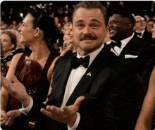 a man in a tuxedo with a mustache is clapping in a crowd of people .