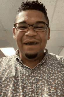 a man wearing glasses and a patterned shirt smiles