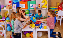 a group of children are sitting around a table playing with paints and balloons