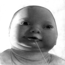 a black and white photo of a baby with a stick in his mouth