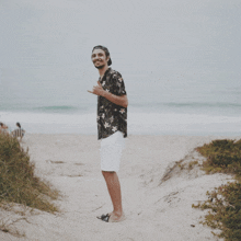 a man in a hawaiian shirt and white shorts stands on a beach